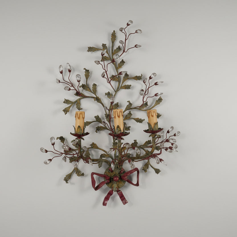 A pair of French tole wall sconces with a green and brown color scheme, featuring metal handles and artificial leaves, mounted on a wall.