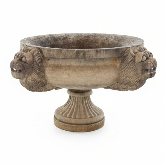 Decorative stone bowl with lion heads on a white wall
