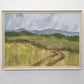 A landscape painting depicting a pathway in a field with a mountain range in the background and a blue sky overhead, framed and hanging on a wall.