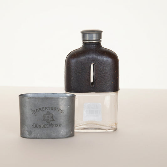 A vintage hip flask and its lid, both with embossed text, the flask is made of metal and the lid has a plastic replacement.