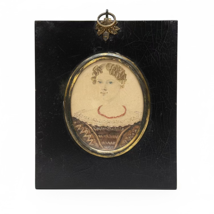 Small portrait in a black frame with a decorative border, placed on a surface with books in the background.