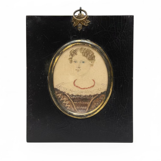 Small portrait in a black frame with a decorative border, placed on a surface with books in the background.
