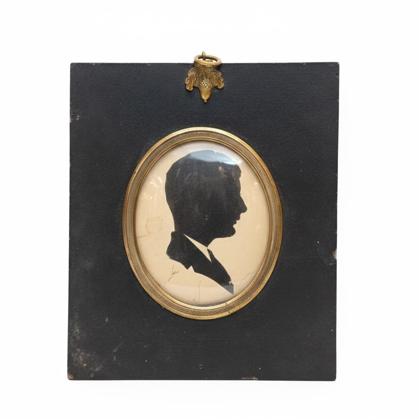 Silhouette portrait in a black frame with gold border on a cluttered surface.